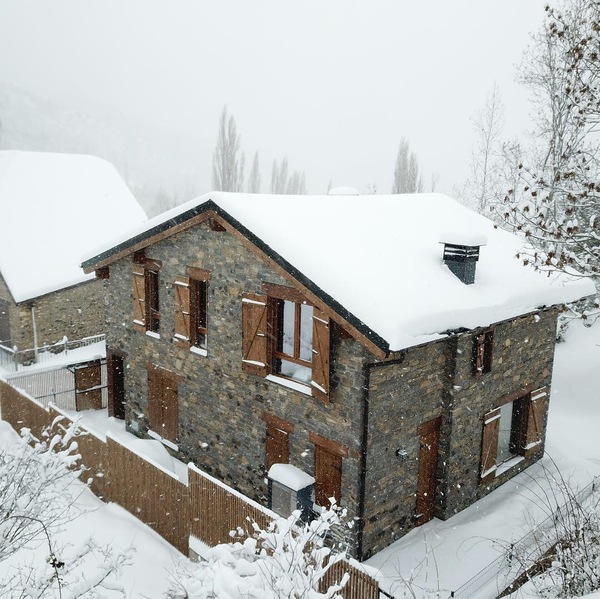 vivienda modular acabada en piedra exterior construida en jaca en paisaje de invierno con capa gruesa de nieve en el tejado